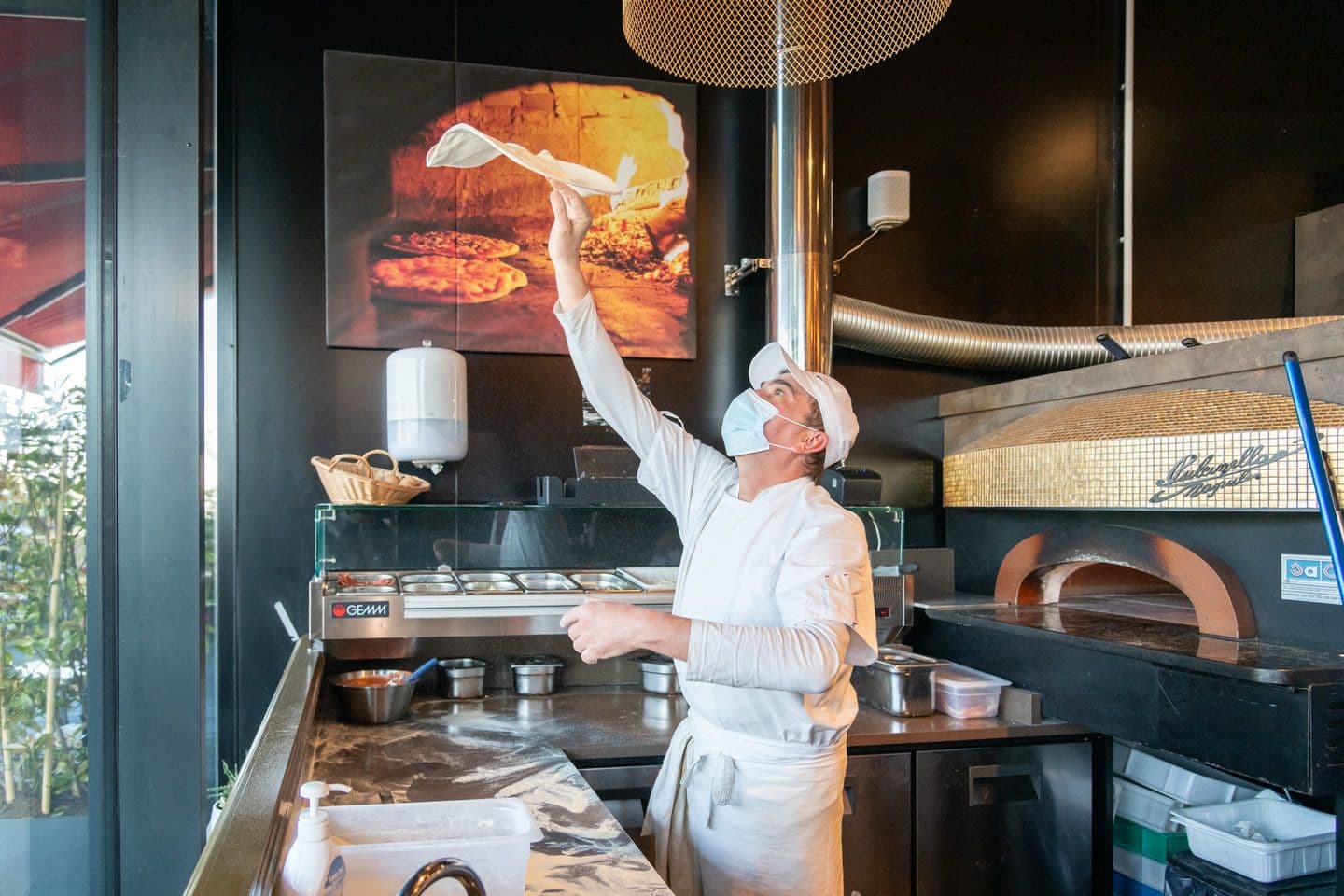 Pizzaiolo qui lève la pâte à pizza en l'air au restaurant Dai Cugini du Marché de Rungis